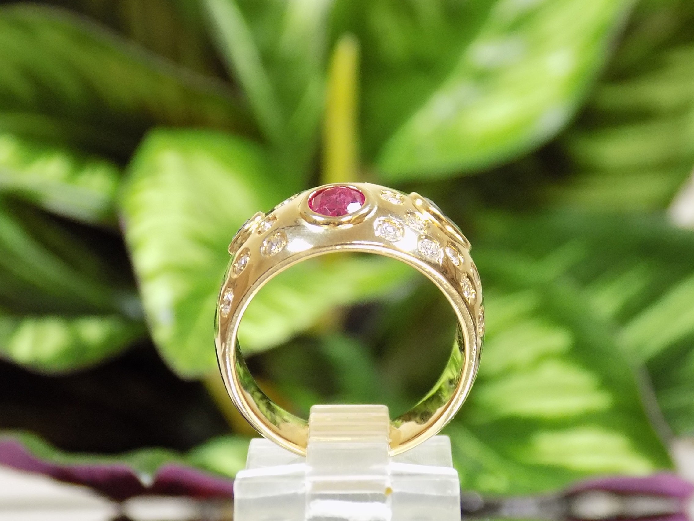 This is a women's estate ring with 2.50ct total weight ruby, sapphire, and diamonds set in 18K yellow gold with a green leafy background from a side view.