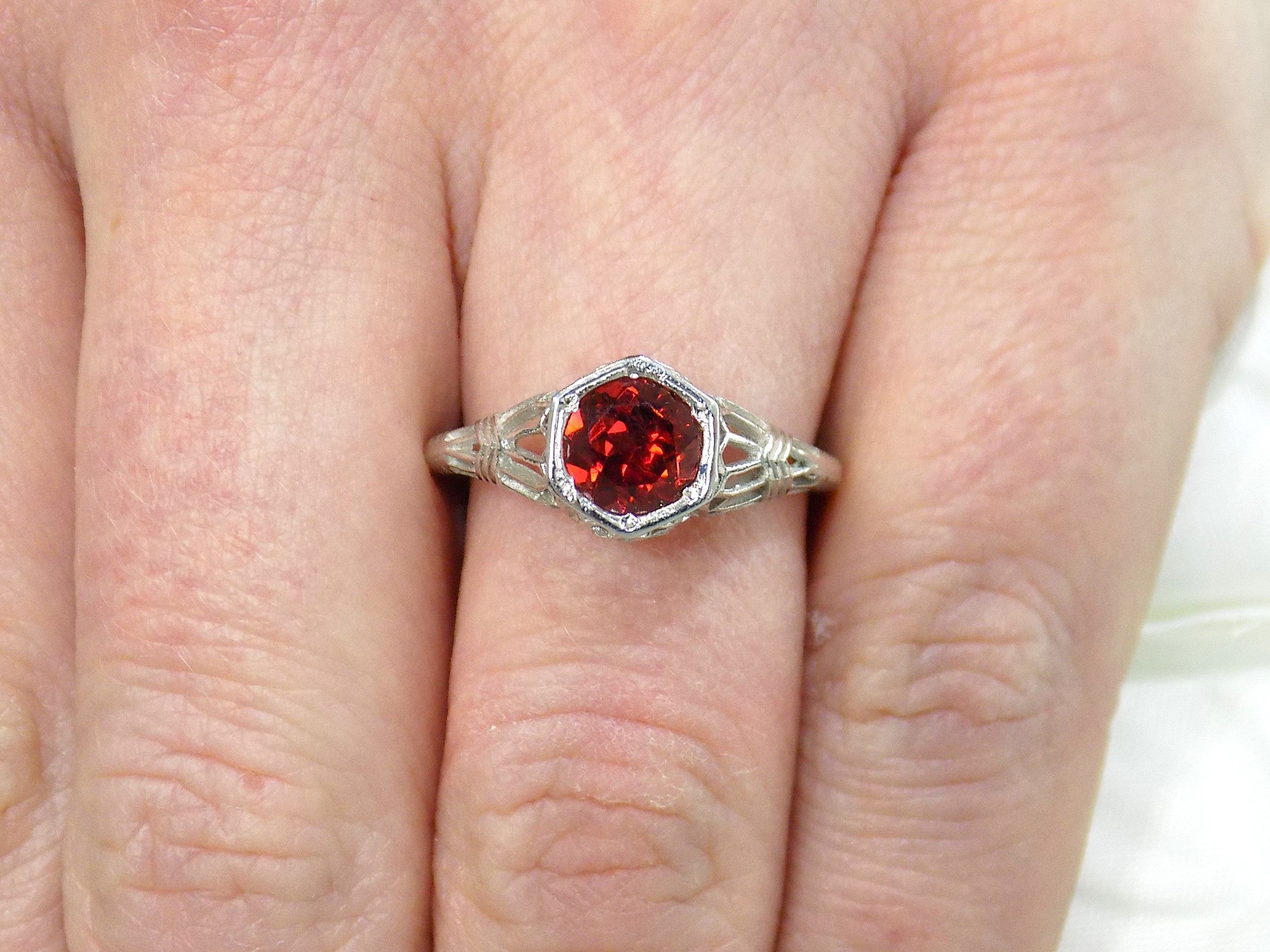 This is a 1.00ct natural garnet ring in a filigree Victorian style in 10K white gold on a ladies finger.