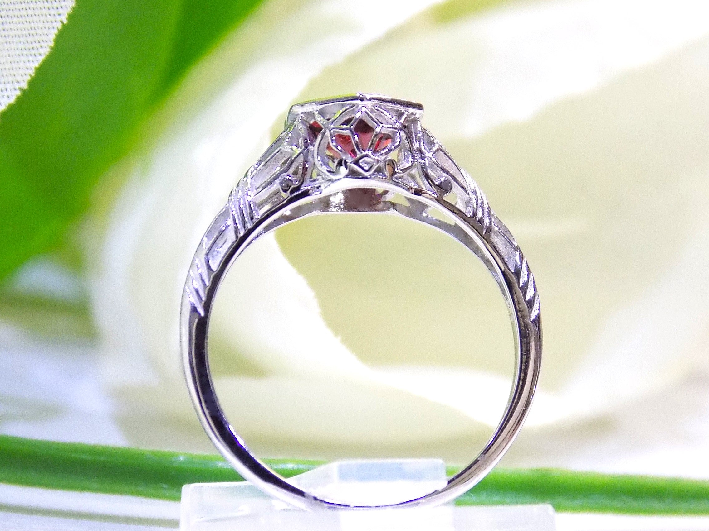 This is a 1.00ct natural garnet ring in a filigree Victorian style in 10K white gold side view with a white and green background.