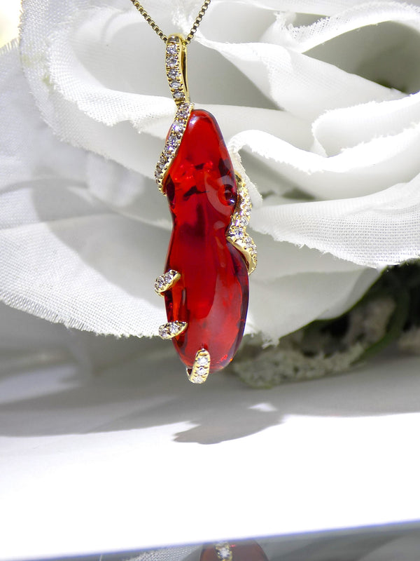 This is a women's custom made necklace with a 6.63ct red fire opal uncut but polished in a custom built 14K yellow gold mounting with .25ct round diamonds making it a 6.88ct total weight with a white floral background.