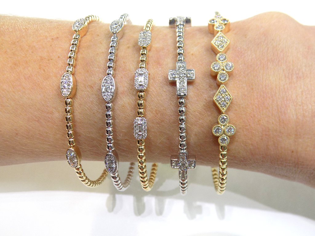 These are 5 natural diamond flex bangles.  Two are in white gold and three are in yellow gold. All stacked on a ladies wrist with a white background.