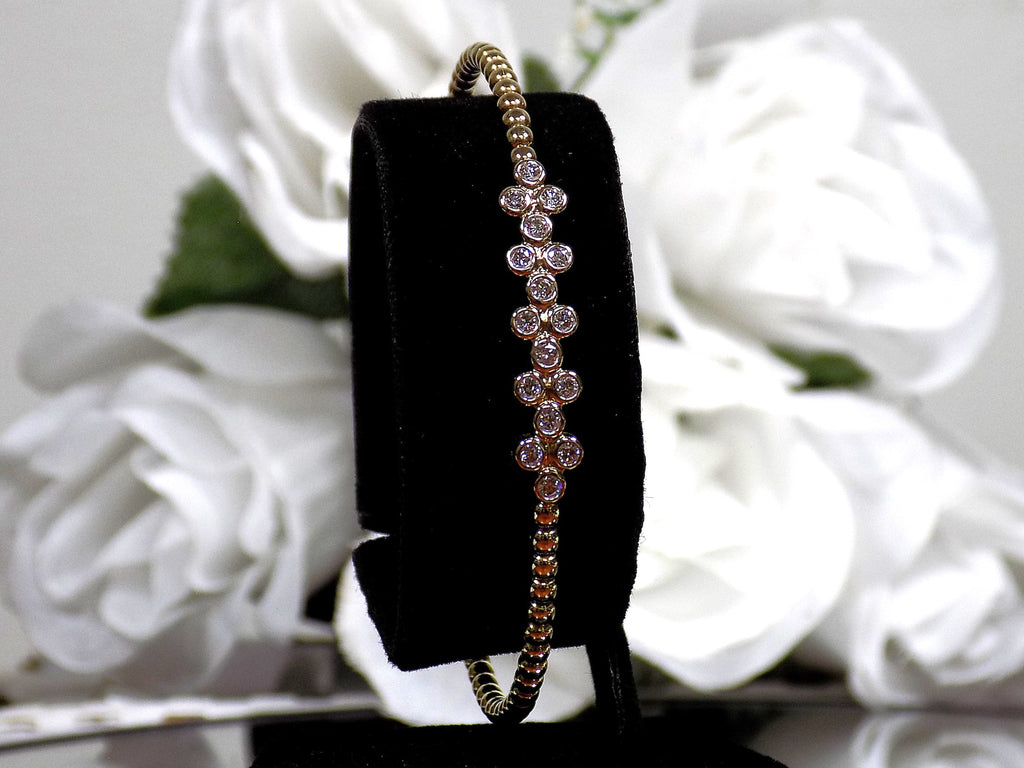 This is a .50ct natural round brilliant diamond flex bangle in 10K yellow gold on a black display with a white floral background.
