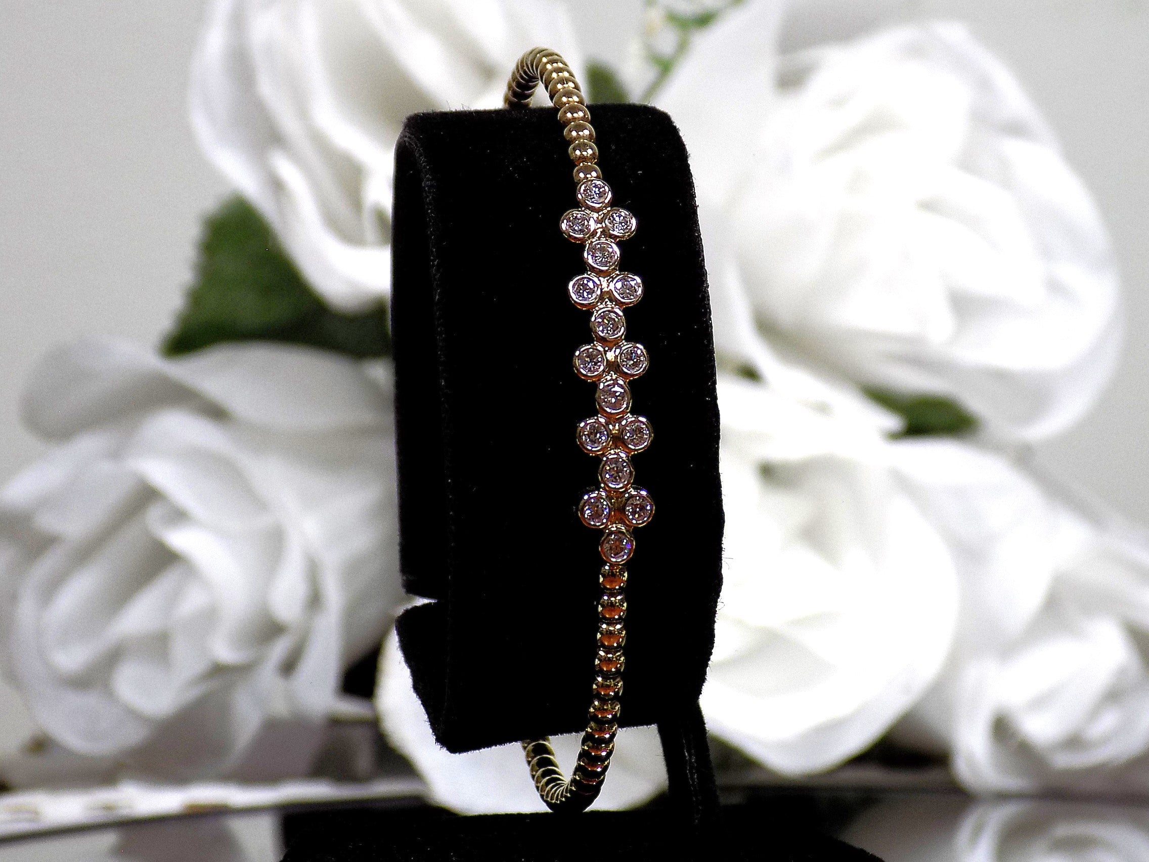 This is a .50ct natural round brilliant diamond flex bangle in 10K yellow gold on a black display with a white floral background.