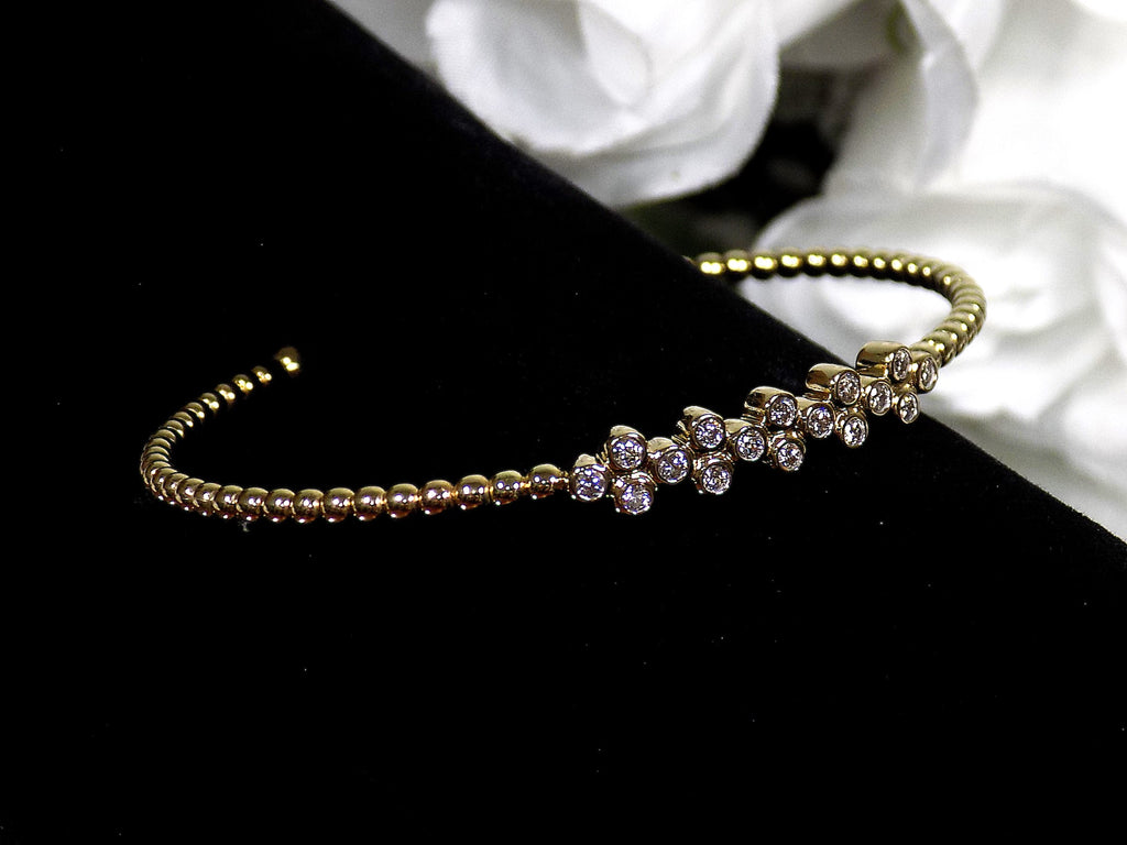 This is a .50ct natural round brilliant diamond flex bangle in 10K yellow gold on a black display with a white floral background.