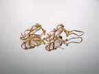 These are genuine large elongated freshwater pearl earrings with omega backs in yellow gold displayed on their side to see the posts and backs on a mirrored background.