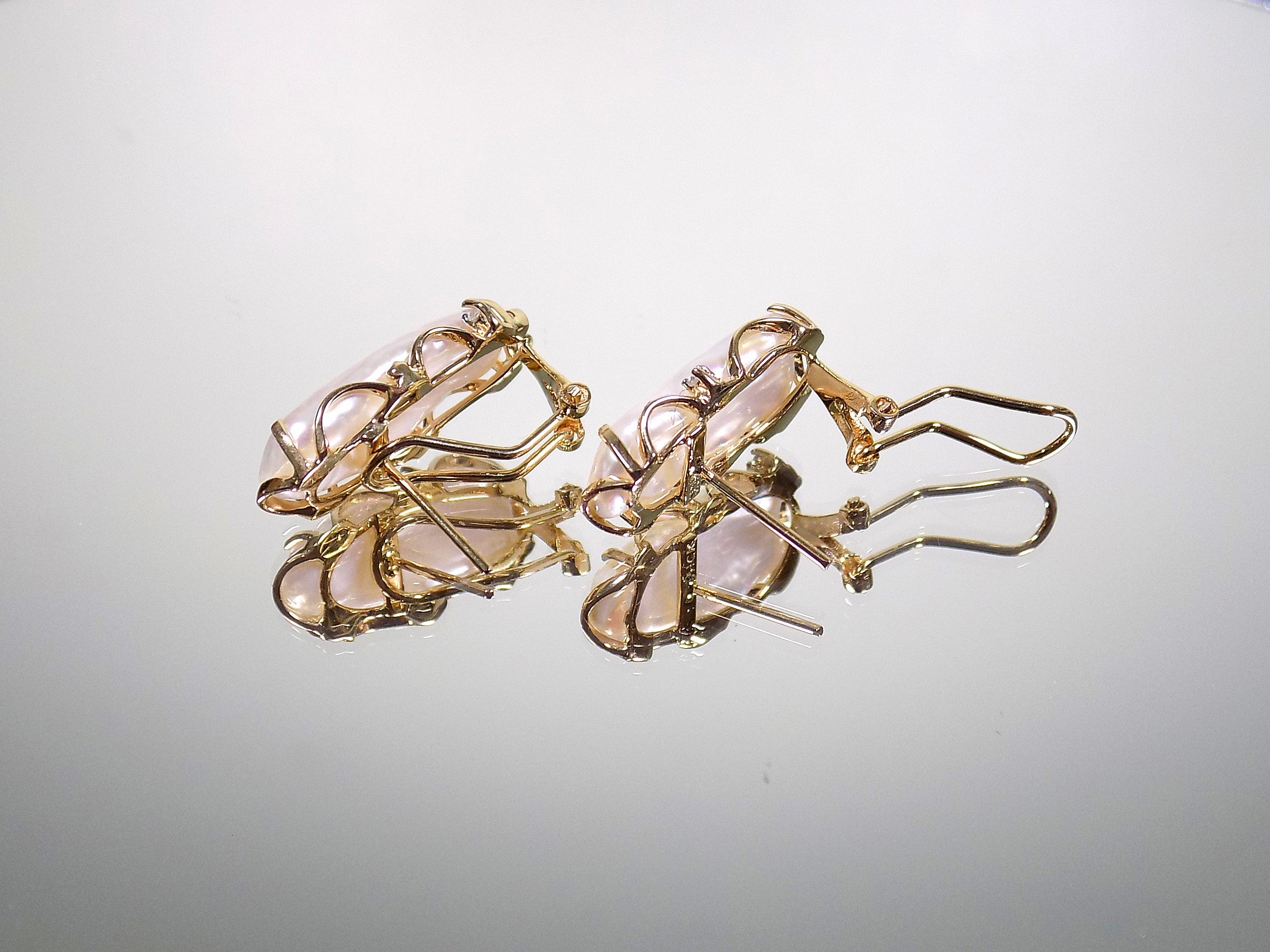 These are genuine large elongated freshwater pearl earrings with omega backs in yellow gold displayed on their side to see the posts and backs on a mirrored background.