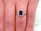 This is an emerald cut genuine garnet ring surrounded by natural diamonds in white gold and fully restored to like new shown on a ladies' finger.
