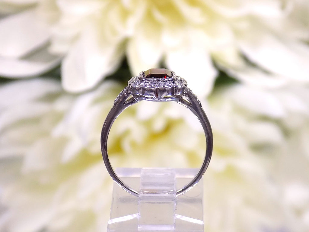This is side view of an emerald cut genuine garnet ring surrounded by natural diamonds in white gold and fully restored to like new with mirrored flowery background.