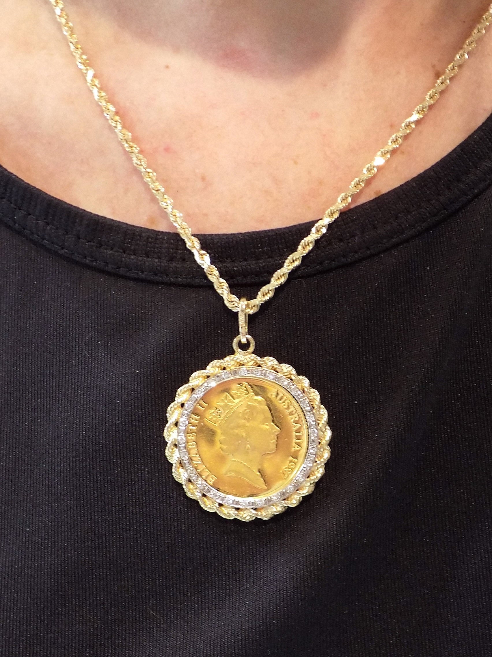 This is a vintage 1987 Australian $200 gold coin with a yellow gold rope and diamond bezel pendant shown hanging on a rope chain on a woman's neck.