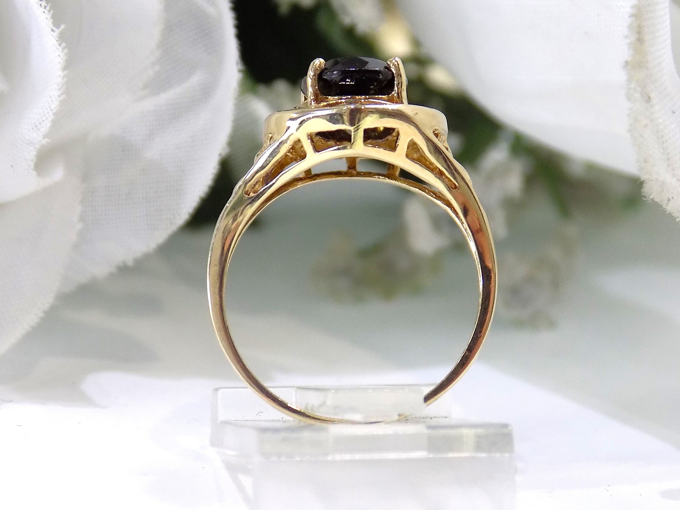 This is a women's natural green tourmaline ring with a 1.70ct genuine oval shape green tourmaline set in a filigree style mounting in 10K yellow gold with a white floral background shown from a side view.