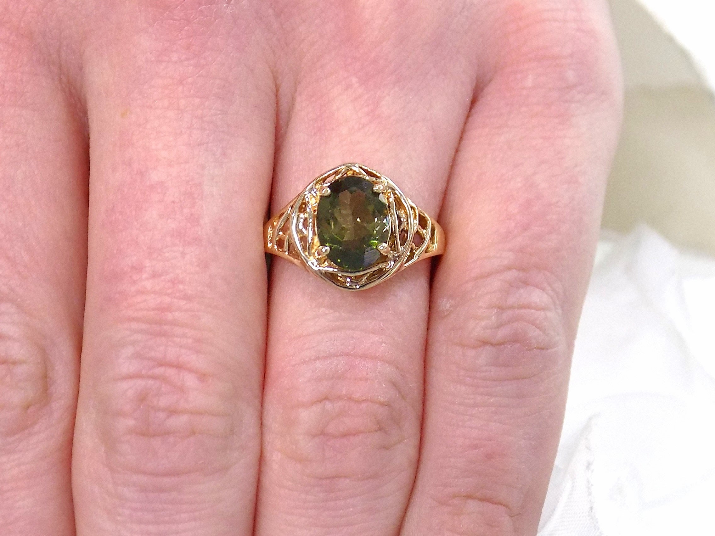 This is a women's natural green tourmaline ring with a 1.70ct genuine oval shape green tourmaline set in a filigree style mounting in 10K yellow gold shown on a women's finger.