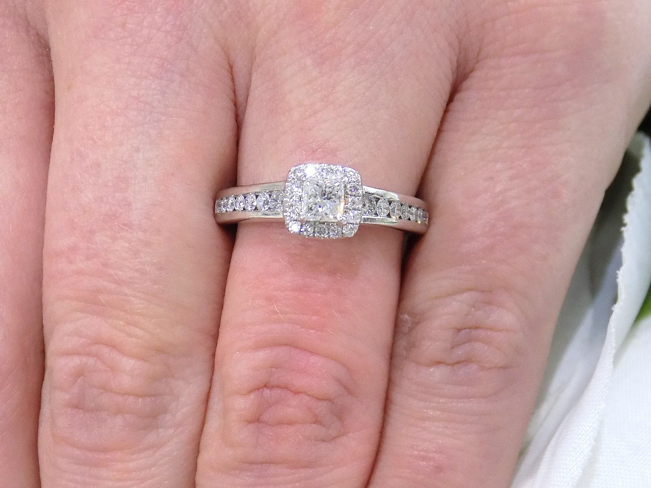 This is a halo style .50ct total weight natural princess cut diamond ring in white gold shown on a woman's finger.