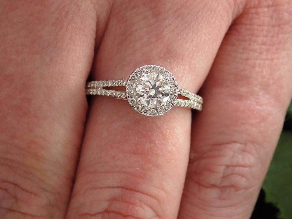 This is a halo style natural .75ct tw round diamond ring shown on a woman's finger.
