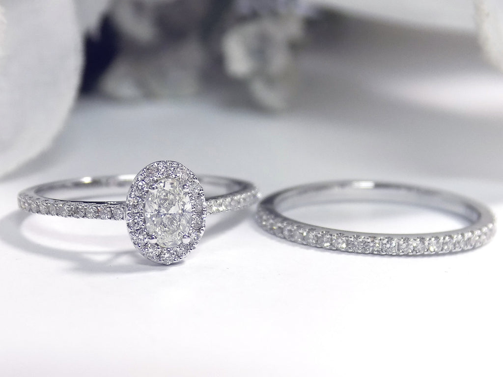 This is a .73ct total weight 2-piece halo style oval shape natural diamond wedding set with engagement ring and matching band in white gold with a white background.