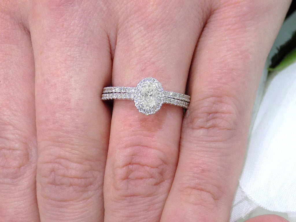 This is a .73ct total weight 2-piece halo style oval shape natural diamond wedding set with engagement ring and matching band in white gold shown on a woman's finger.