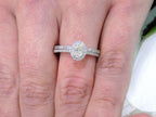 This is a .73ct total weight 2-piece halo style oval shape natural diamond wedding set with engagement ring and matching band in white gold shown on a woman's finger.