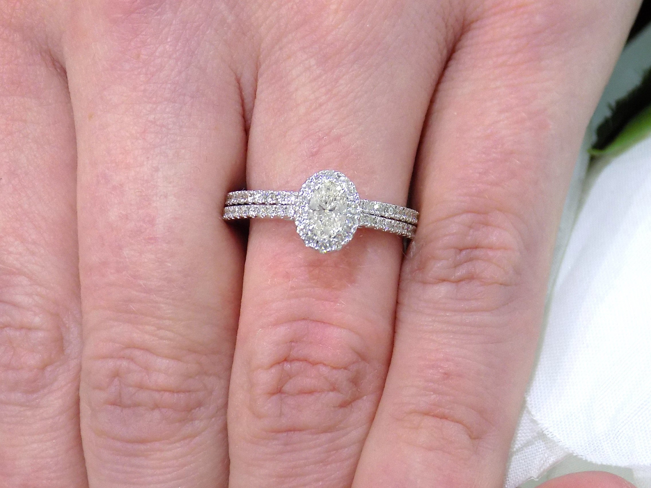 This is a .73ct total weight 2-piece halo style oval shape natural diamond wedding set with engagement ring and matching band in white gold shown on a woman's finger.