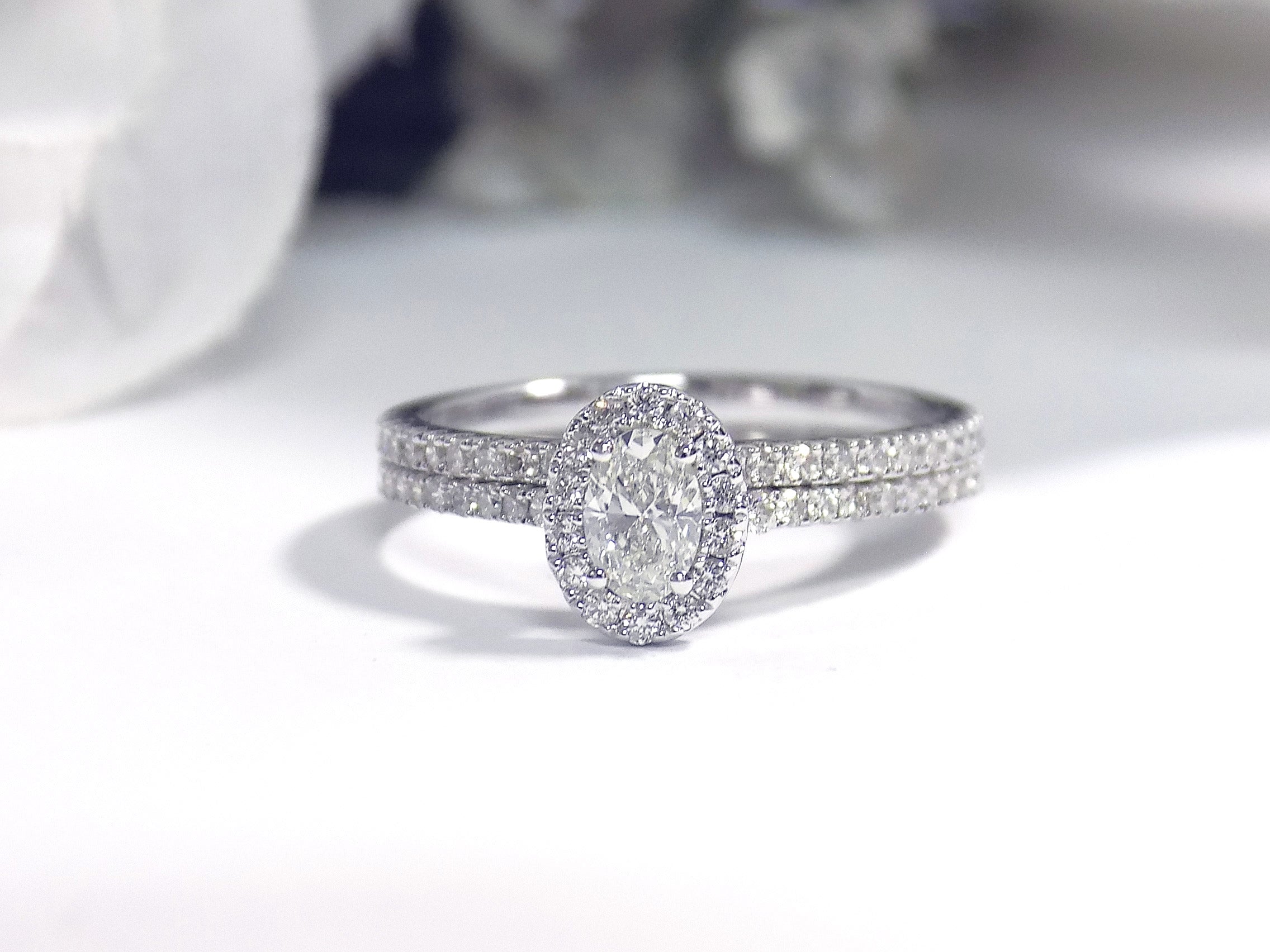 This is a .73ct total weight 2-piece halo style oval shape natural diamond wedding set with engagement ring and matching band in white gold with a white background.