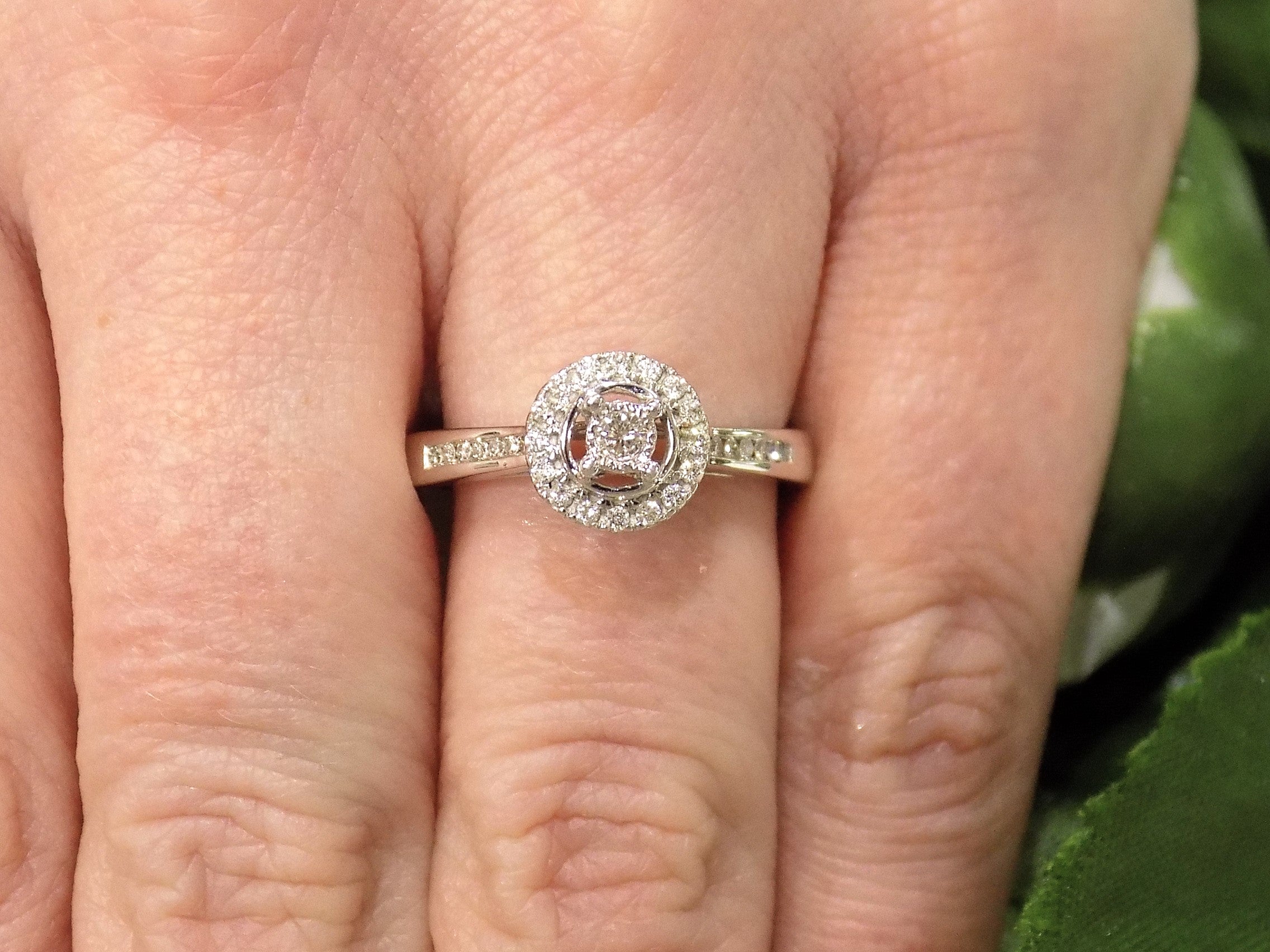 Ladies' halo style small round diamond ring in white gold shown on a woman's finger.