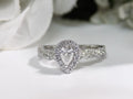 This is a halo style .82ct total weight natural pear shape diamond ring with infinity style band in white gold with a white background.