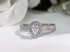 This is a halo style .82ct total weight natural pear shape diamond ring with infinity style band in white gold with a white background.