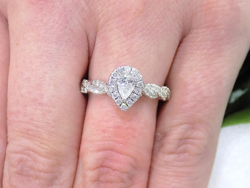 This is a halo style .82ct total weight natural pear shape diamond ring with infinity style band in white gold shown on a woman's finger.