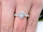 This is a halo style .82ct total weight natural pear shape diamond ring with infinity style band in white gold shown on a woman's finger.