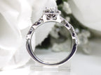 This is a side view of a halo style .82ct total weight natural pear shape diamond ring with infinity style band in white gold with a white background.