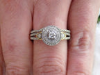 This is a halo style 2-piece wedding set ring with matching band in white gold with yellow gold accents shown on a ladies' finger.