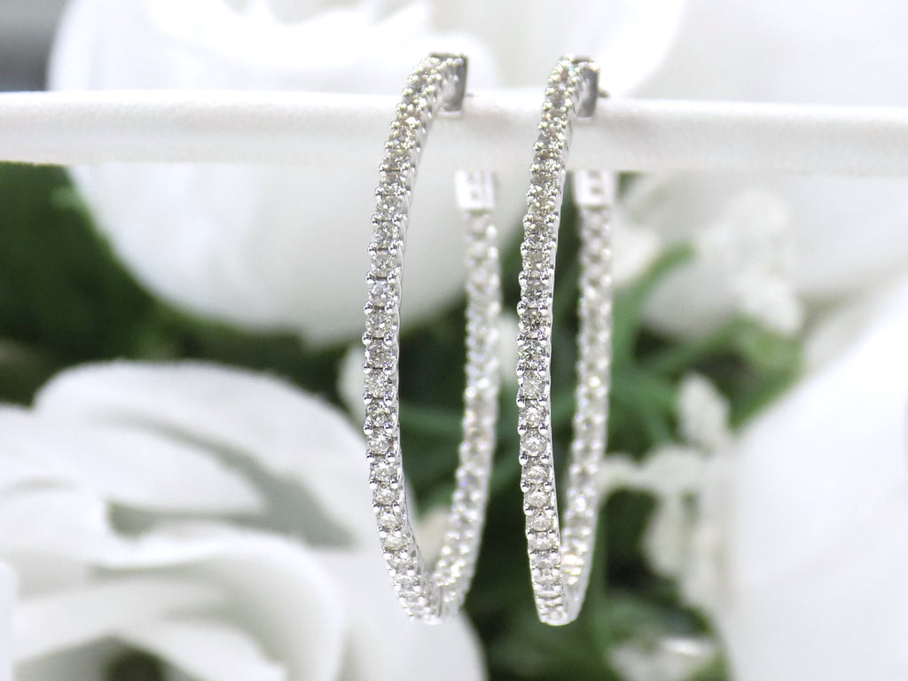 These are very large 1 1/2" in diameter 2.00ct round brilliant diamond hoop earrings in 14K white gold on a white pole with a white floral background.