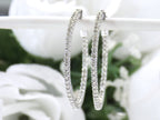 These are very large 1 1/2" in diameter 2.00ct round brilliant diamond hoop earrings in 14K white gold on a white pole with a white floral background.
