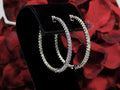 These are very large 1 1/2" in diameter 2.00ct round brilliant diamond hoop earrings in 14K white gold. on a black stand with a red floral background.