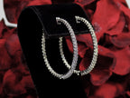 These are very large 1 1/2" in diameter 2.00ct round brilliant diamond hoop earrings in 14K white gold. on a black stand with a red floral background.