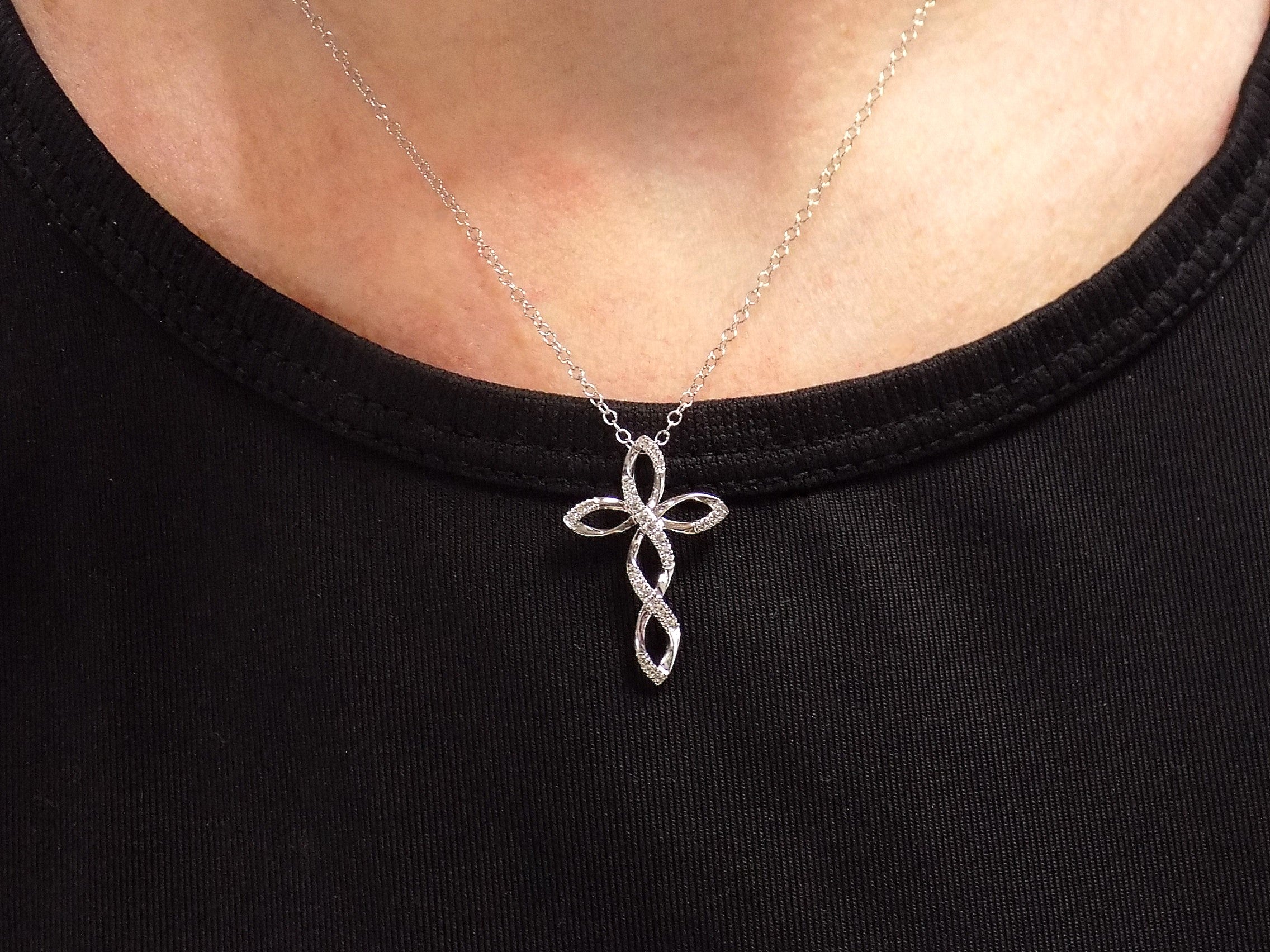 This is an infinity style natural diamond cross necklace in white gold on a ladies neck.