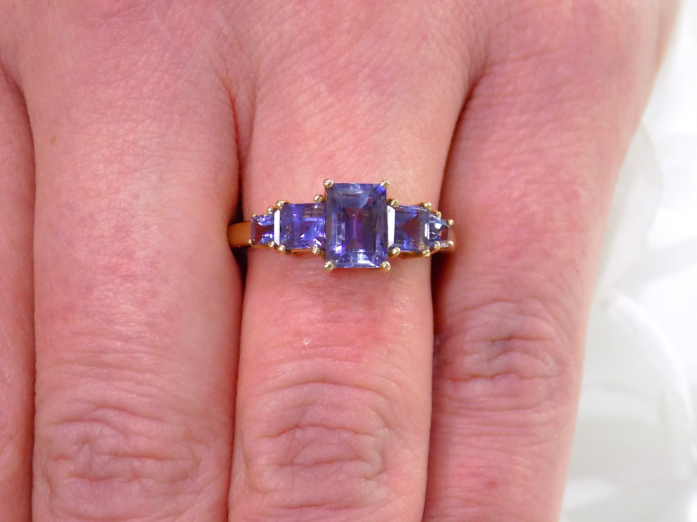 This a 5-stone genuine emerald cut iolite ring in yellow gold from our estate collection in like new condition shown on a woman's finger.