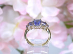 This a side view of a 5-stone genuine emerald cut iolite ring in yellow gold from our estate collection in like new condition shown with a pink flowery background.