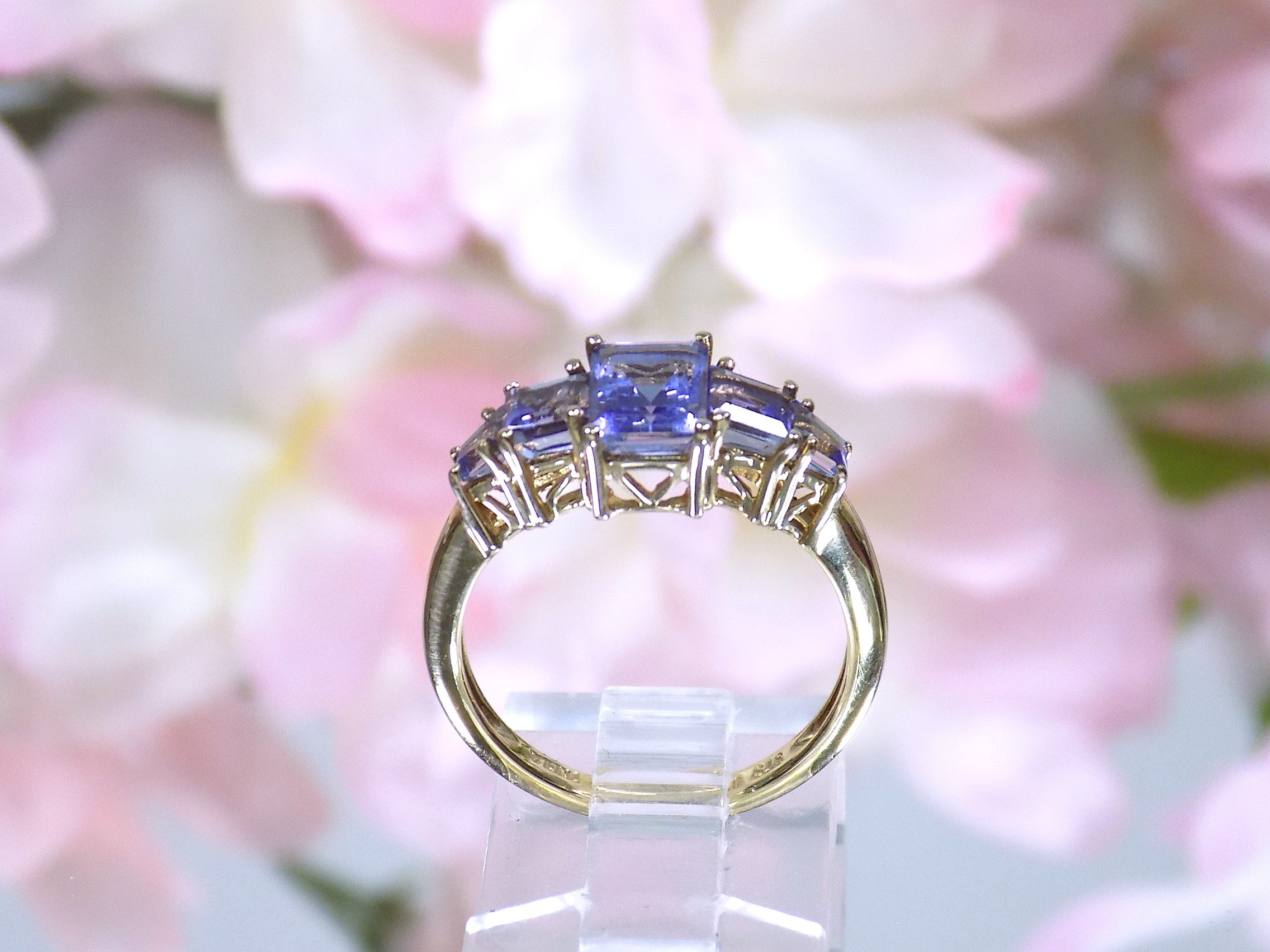 This a side view of a 5-stone genuine emerald cut iolite ring in yellow gold from our estate collection in like new condition shown with a pink flowery background.
