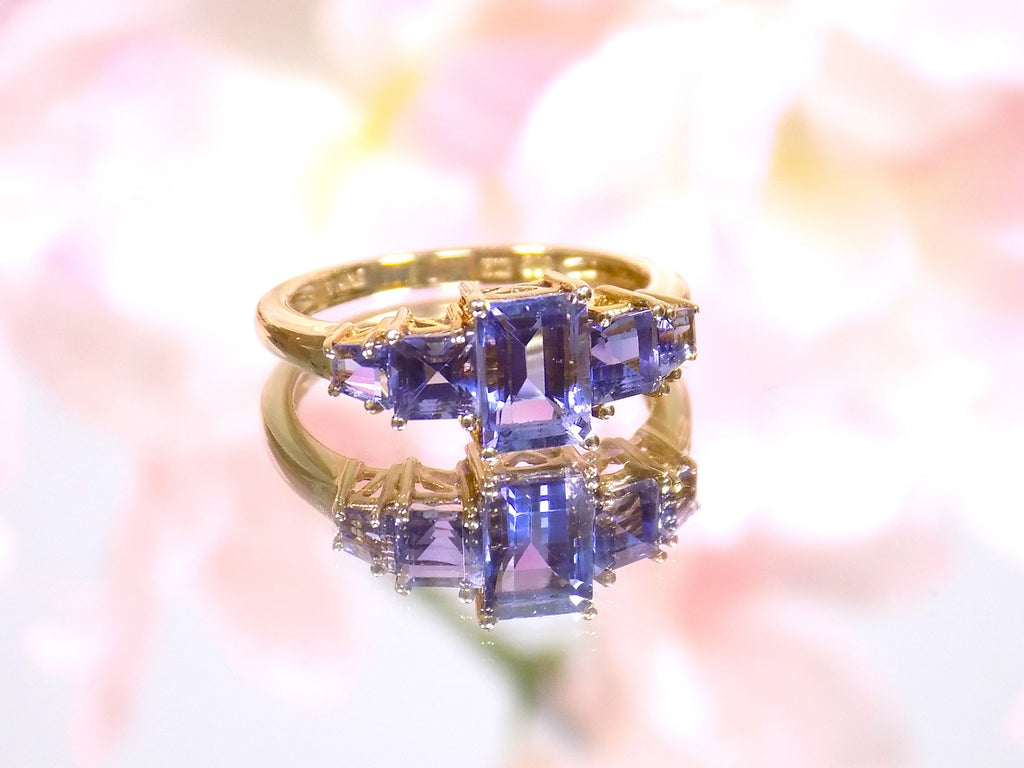 This a 5-stone genuine emerald cut iolite ring in yellow gold from our estate collection in like new condition shown with a pink flowery background.