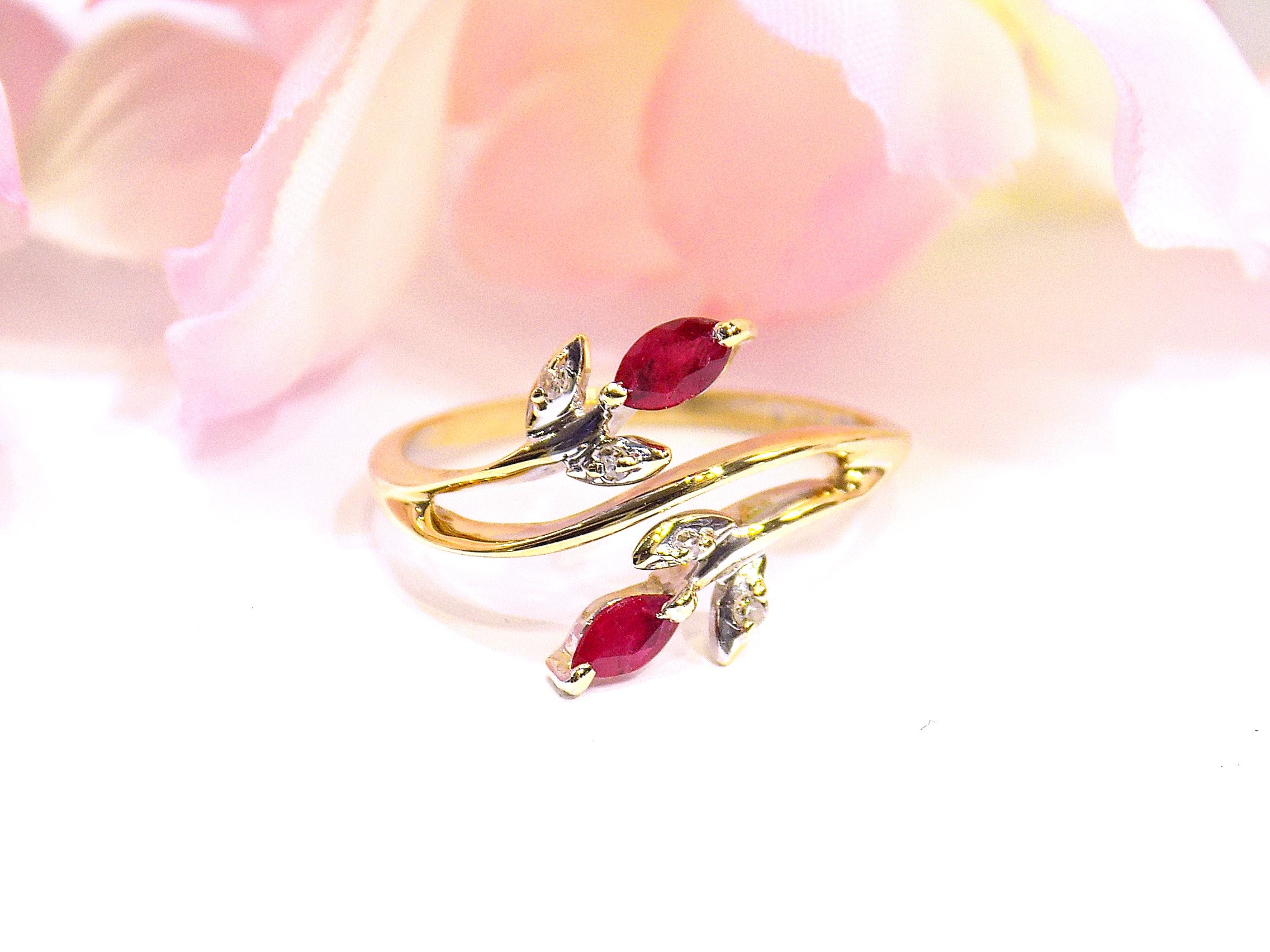 This is a .32ct total weight marquise shaped natural ruby and diamond ring in 10K yellow gold with a white and pink floral background.