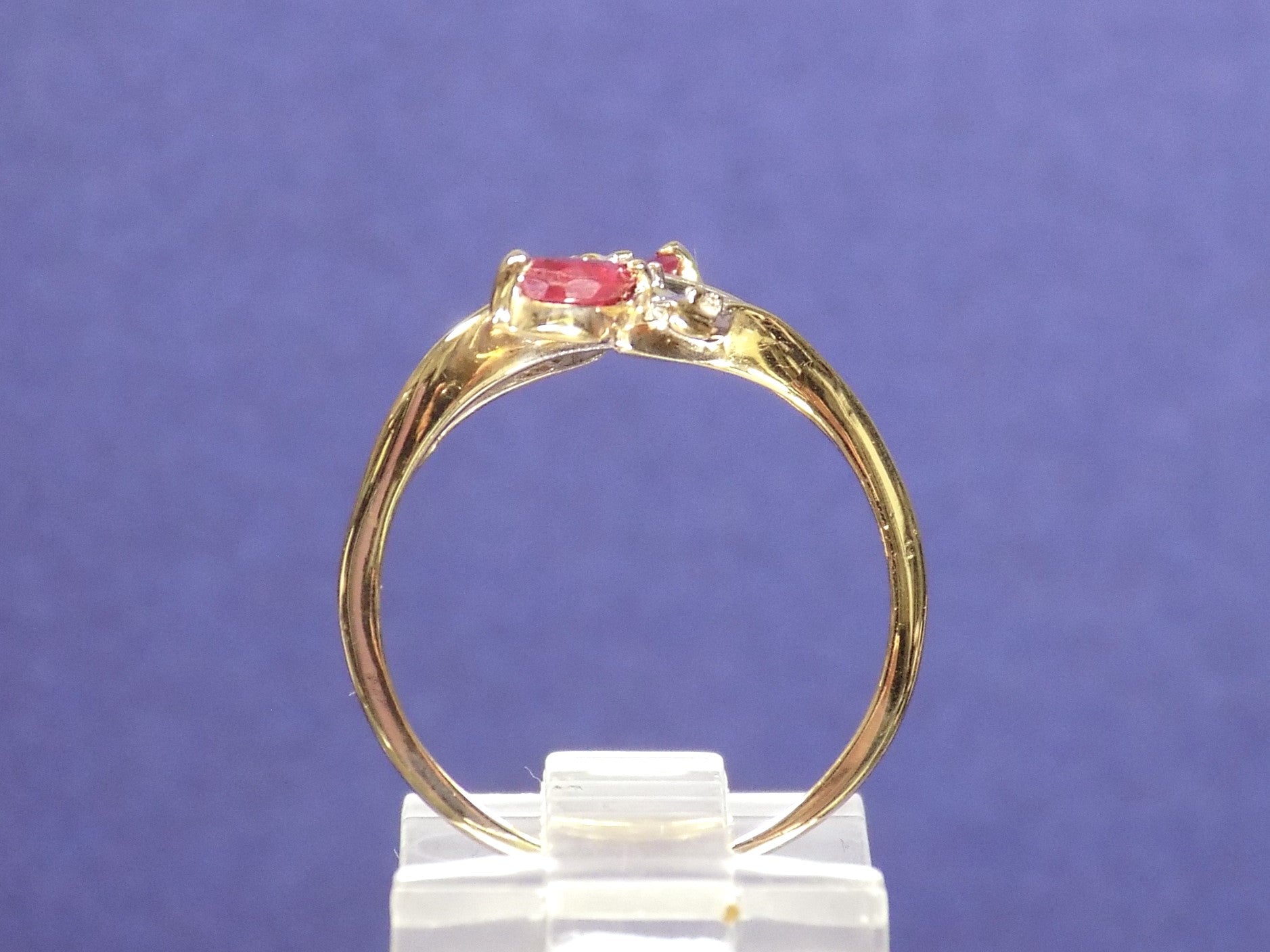 This is a .32ct total weight marquise shaped natural ruby and diamond ring in 10K yellow gold side view with a bluish/purple background.