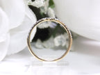 This is a side view of a diamond band that matches an oval shape diamond engagement ring in yellow gold with white gold prongs and a white backgroud.