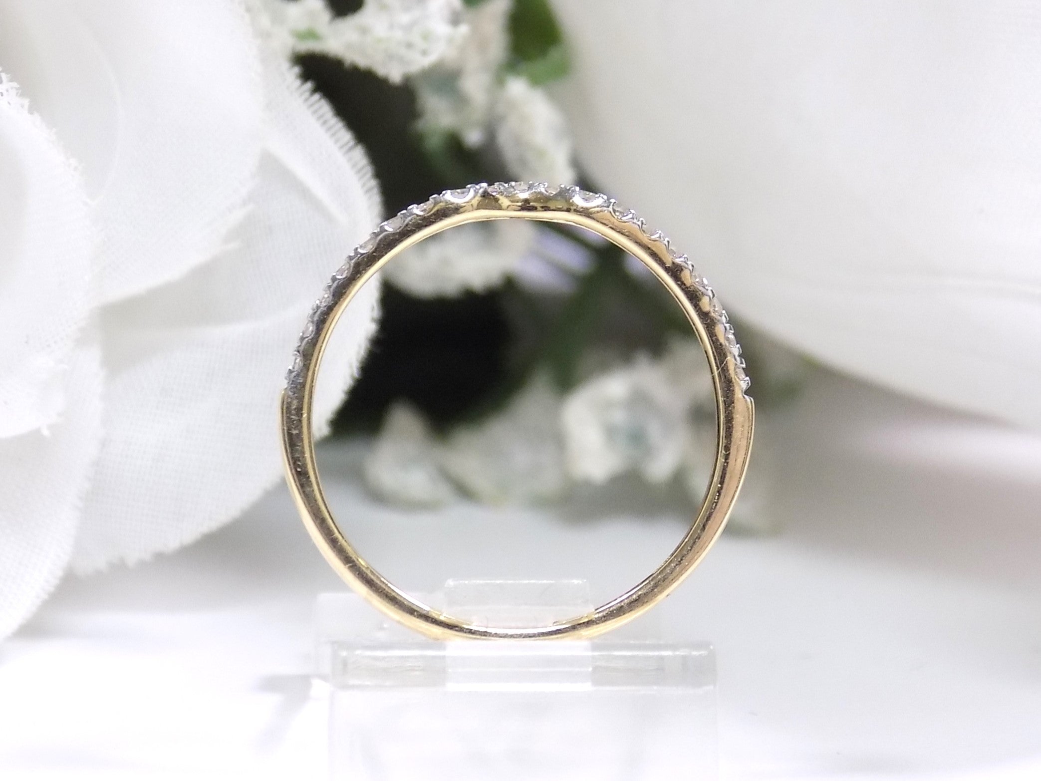 This is a side view of a diamond band that matches an oval shape diamond engagement ring in yellow gold with white gold prongs and a white backgroud.