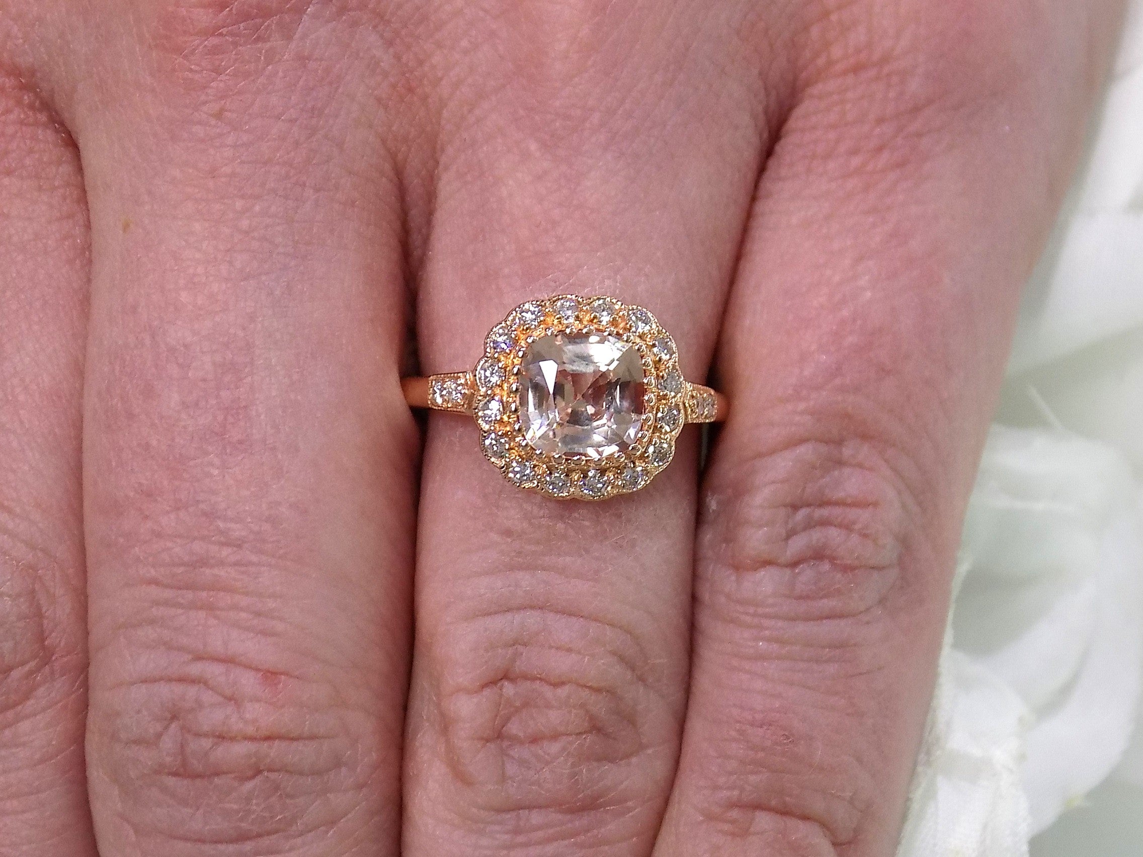 This is a women's ring with 1.94ct natural cushion cut morganite in the center surrounded by .30ct in natural round diamond accents in 14K rose gold sitting on a woman's finger.