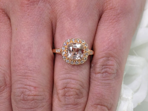 This is a women's ring with 1.94ct natural cushion cut morganite in the center surrounded by .30ct in natural round diamond accents in 14K rose gold sitting on a woman's finger.