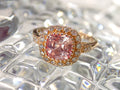 This is a women's ring with 1.94ct natural cushion cut morganite in the center surrounded by .30ct in natural round diamond accents in 14K rose gold sitting on a textured glass surface.