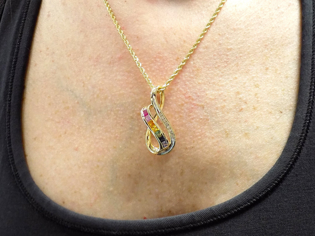 This is a women's slide pendant with 1.38ct total weight natural multicolor natural sapphires and .12ct total weight natural round diamonds in 14K yellow gold on a women's neck with a black shirt.