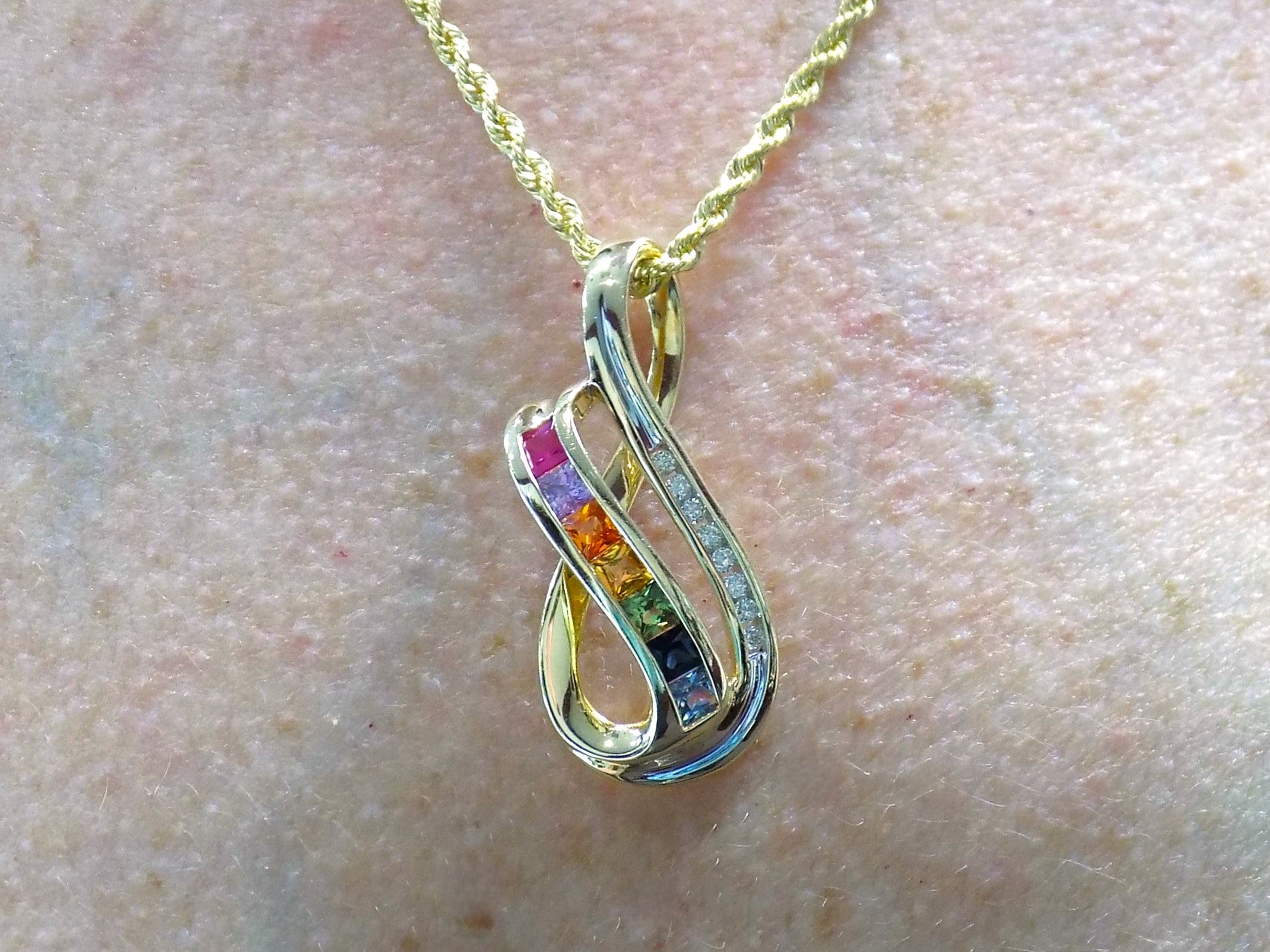 This is a women's slide pendant with 1.38ct total weight natural multicolor natural sapphires and .12ct total weight natural round diamonds in 14K yellow gold on a women's neck.