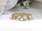 This is a multi shape natural diamond ring including a pea shape, round brilliant, emerald cut, princess cut and oval shape all surrounded by round diamond accents in 10K yellow gold on a white background.