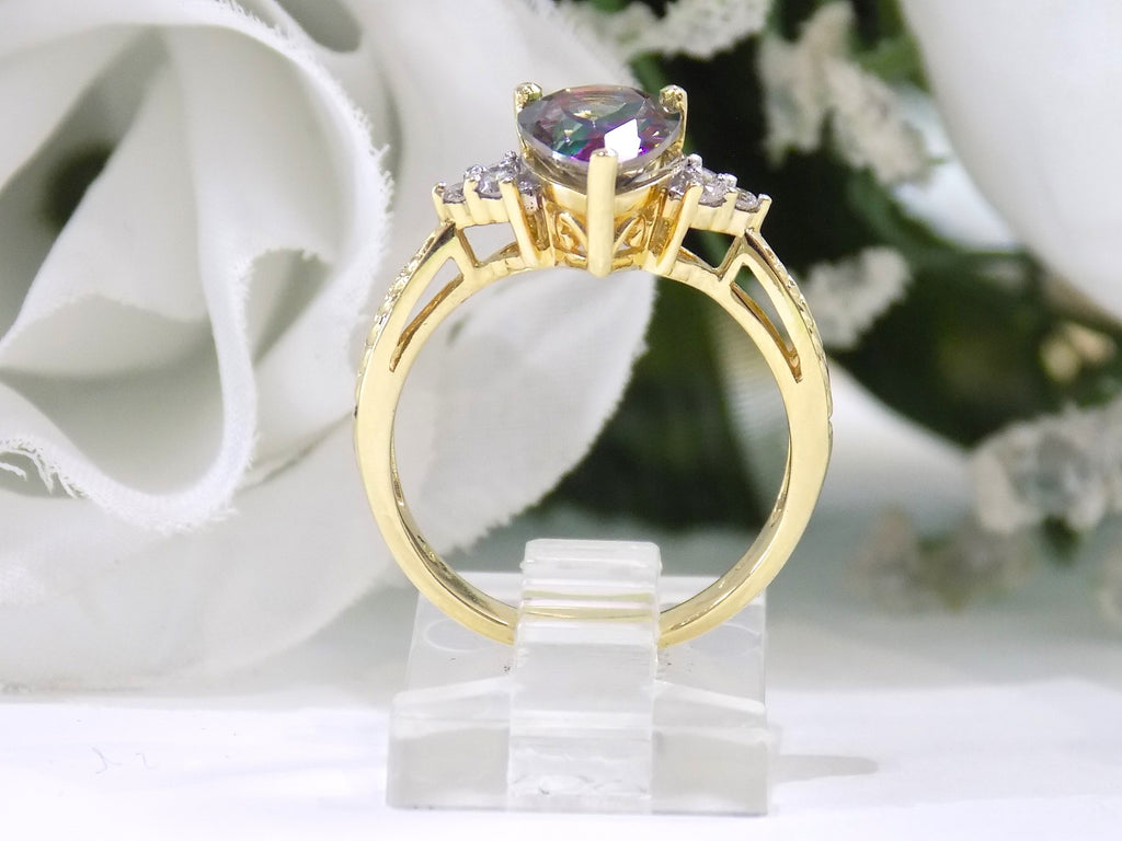 This is a women's ring with a 2.00ct pear shape mystic fire topaz center in green and purple with .12ct natural accent diamonds set in 14K yellow gold on a white surface with a white floral background.