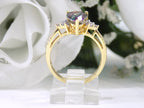 This is a women's ring with a 2.00ct pear shape mystic fire topaz center in green and purple with .12ct natural accent diamonds set in 14K yellow gold on a white surface with a white floral background.